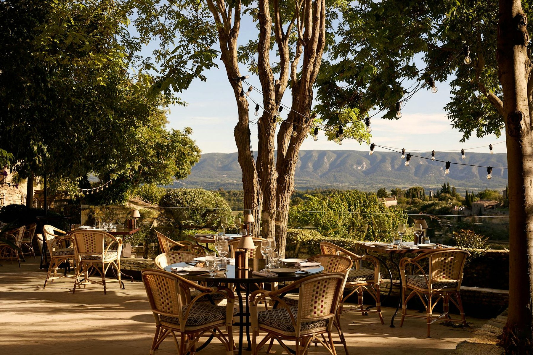 The terrace at golden hour, tables under the trees with the Luberon valley beyond