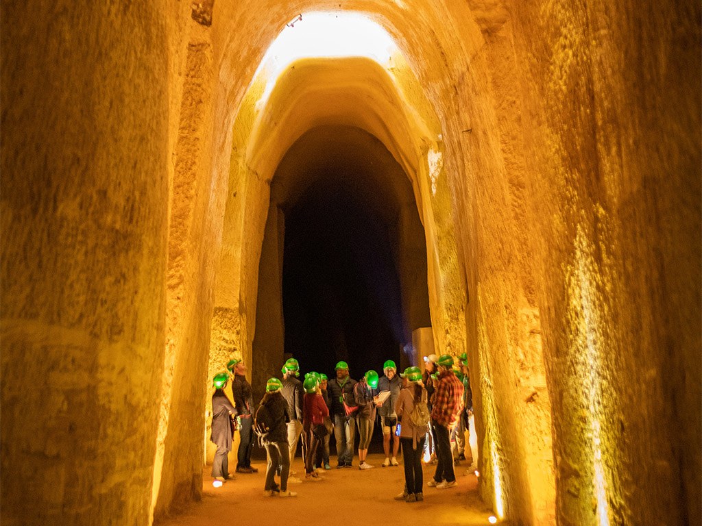 A guided group in the lit ochre galleries, the vaulted tunnel rising above them